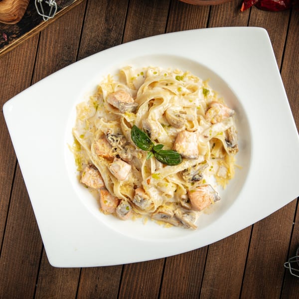 Caruso's creamy fettuccine pasta with salmon, mushrooms, and basil on a white plate.