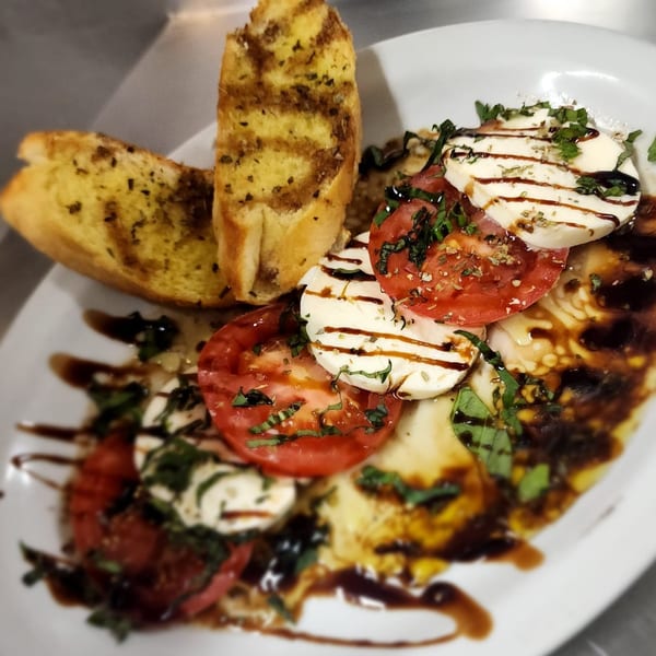 Caruso's Caprese salad with sliced tomatoes, mozzarella, basil, balsamic glaze, and garlic bread.