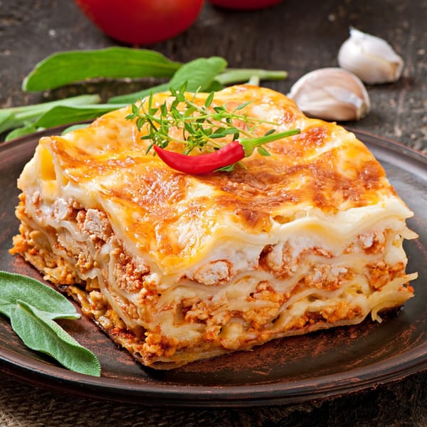 A golden-brown slice of Caruso's Italian lasagna, garnished with a red chili and thyme.