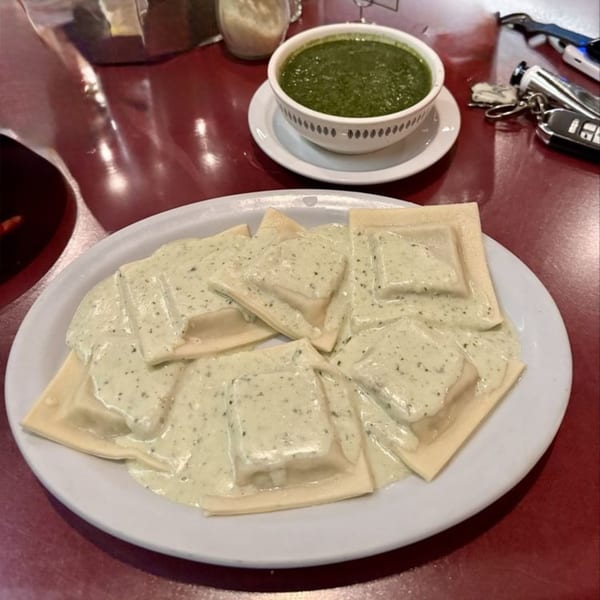 Caruso's ravioli with creamy pesto sauce on a white plate, with a bowl of pesto.