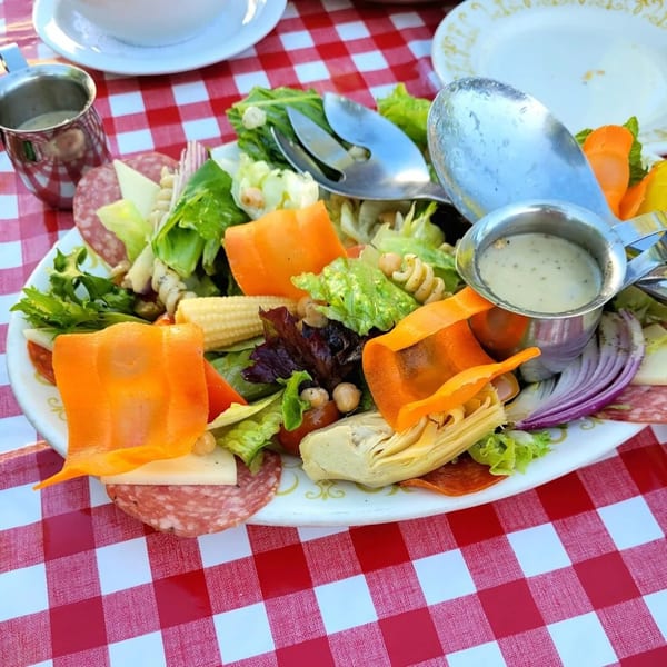 A large Italian salad with salami, cheese, vegetables, and dressing on a red and white checkered tablecloth.