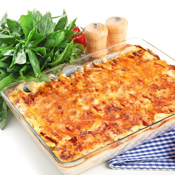 A golden-brown baked pasta dish in a glass pan, with fresh basil, tomatoes, and shakers.